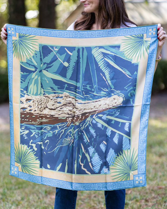 Person holding a large blue and green patterned fabric with an alligator design outdoors.