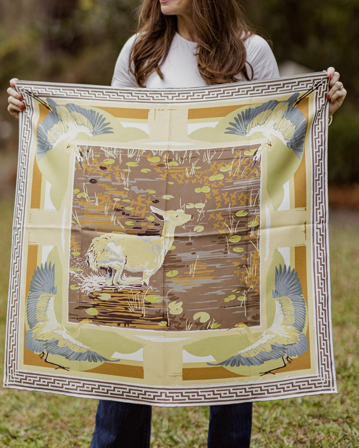 Person holding a large decorative scarf with a nature-themed design outdoors.