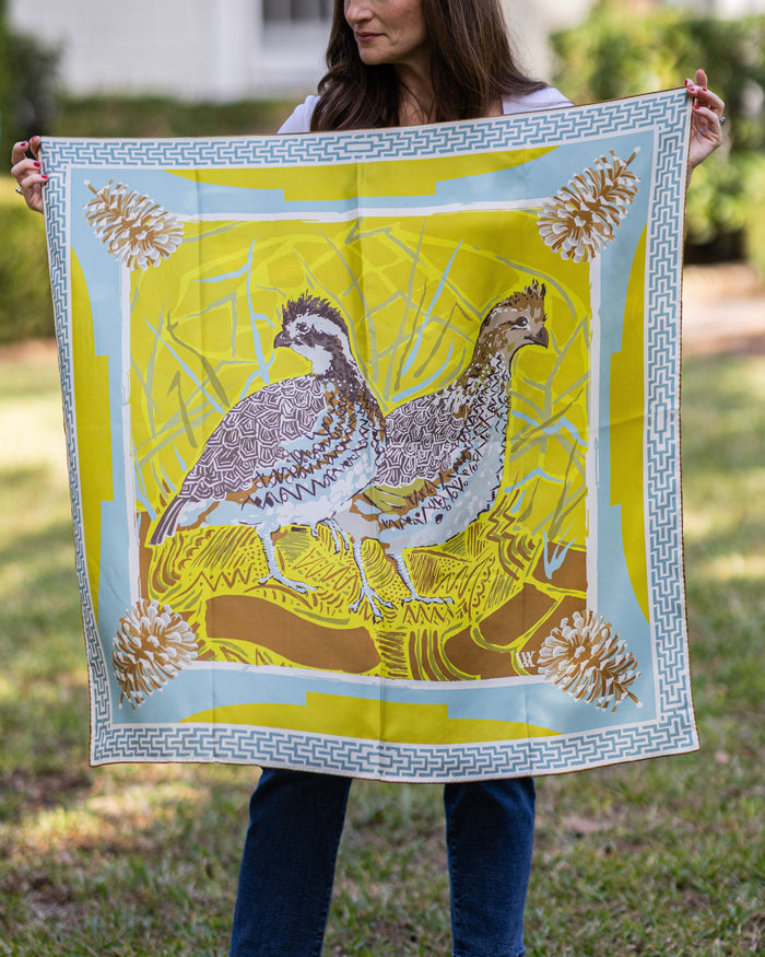Person holding a large silk scarf with a quail and pinecone design outdoors