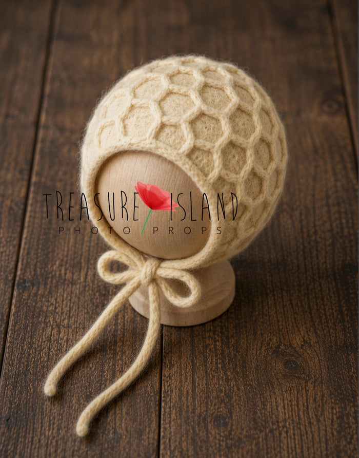handmade newborn bonnet with raised honeycomb felt texture and tieback strings, displayed on dark rustic wooden boards.