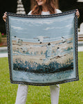Woman holding a silk scarf with birds flying over a marsh and a decorative border.