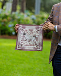 A man in a brown plaid blazer holds up a silk pocket square featuring a hunting dog.