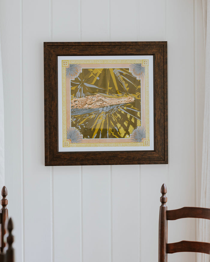 A framed art print featuring a stylized illustration of a alligator in a yellow and green patterned background, hanging on a white paneled wall above a wooden dining table and chairs.