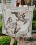 Woman holding a large square scarf with bird design and coastal motif outdoors