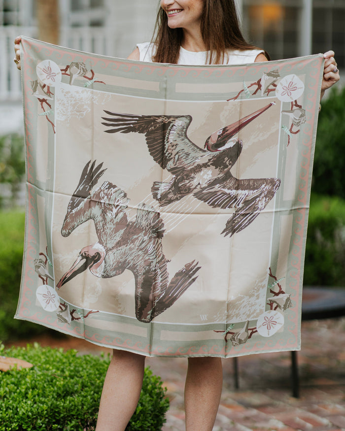 Woman holding a large square scarf with bird design and coastal motif outdoors