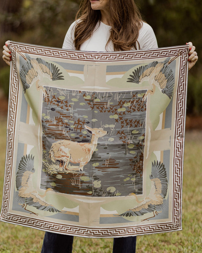 Person holding a large decorative scarf with nature-themed design outdoors.