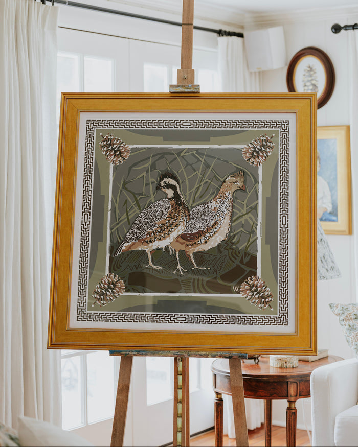 A framed art print featuring two quail birds with pinecones, displayed on a wooden easel.