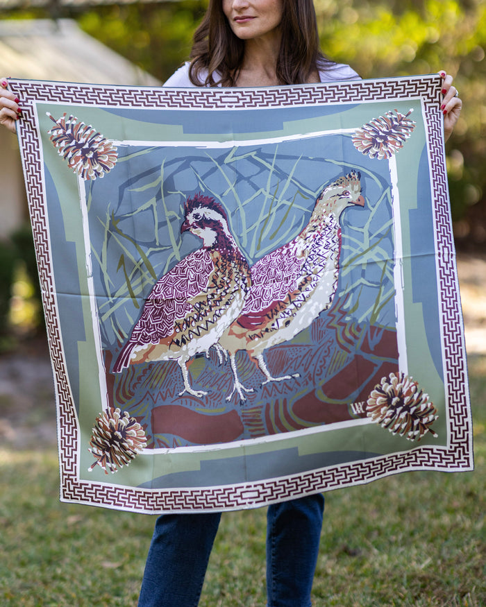 Person holding a large silk scarf with a design of two quail and pinecones.