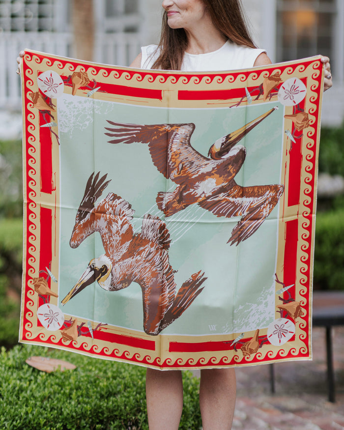 Person holding a large decorative silk scarf with pelican design outdoors.