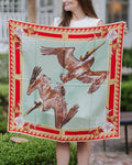 Person holding a large decorative silk scarf with pelican design outdoors.