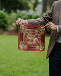 A person outdoors holding up a silk pocket square with  hunting dog illustration and decorative corner details.